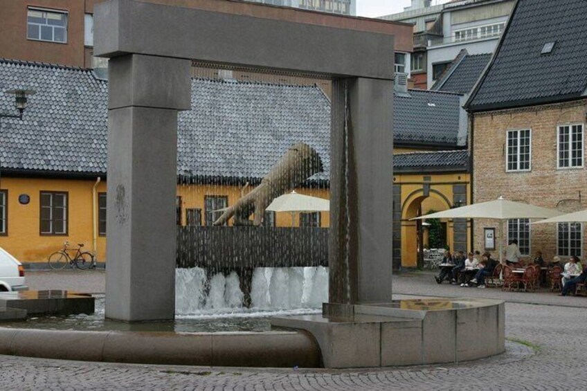 A water feature with a wooden structure, a yellow building, and outdoor seating in the background. 3