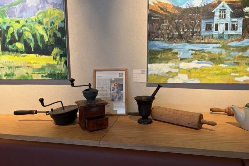 A wooden table with vintage kitchen utensils and two paintings on the wall. 2