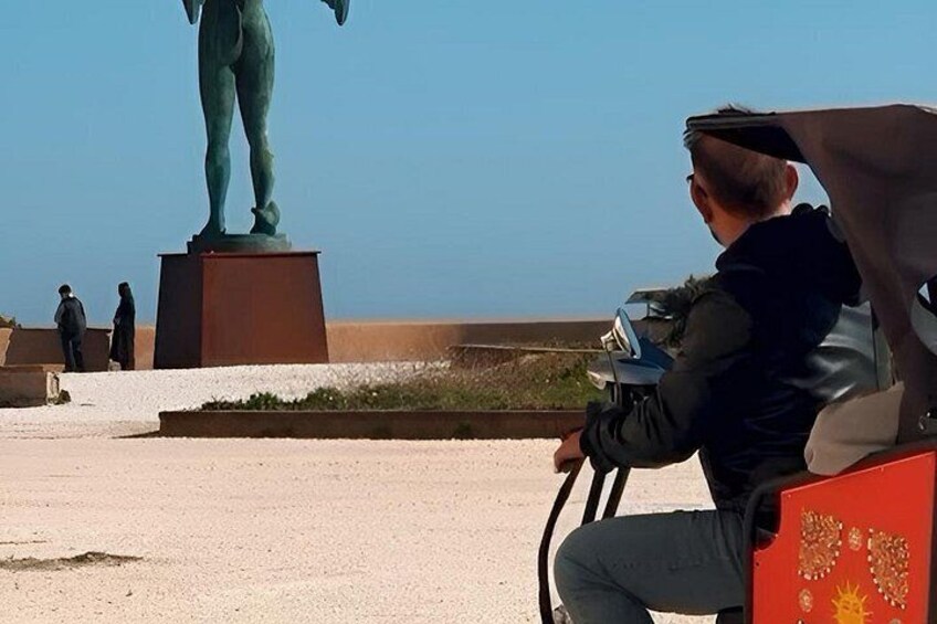 A person sitting on a red chair with a red cushion, a statue in the background, and a clear blue sky. 2