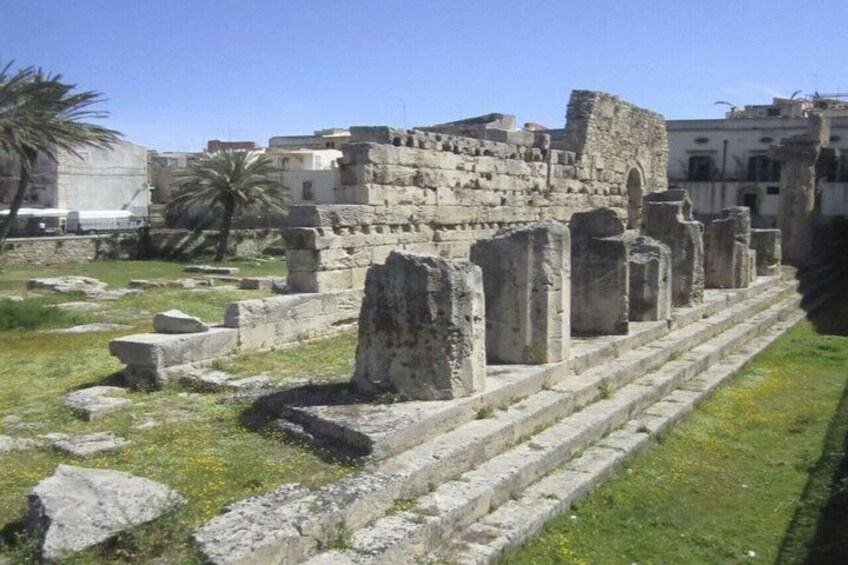 Ancient ruins with stone columns and steps, surrounded by grass and palm trees. 4