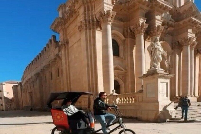 A historic building with classical architecture, a person riding a bicycle, and another person standing near the entrance. 3