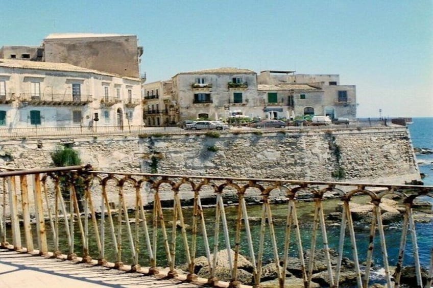 A coastal town with historic buildings, a stone wall, and a metal railing. 5