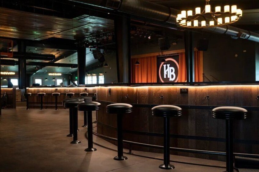 A bar area with stools and a counter, a logo on the wall, and a chandelier. 4