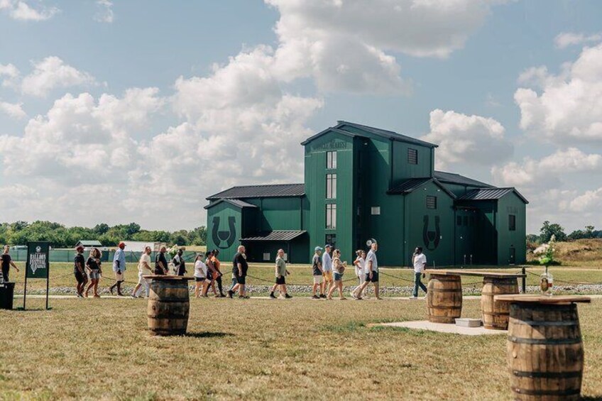 A green building with a horse logo, surrounded by people and barrels in a grassy field. 5