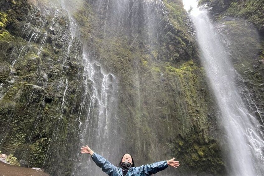 A person standing with arms outstretched in front of a waterfall. 1