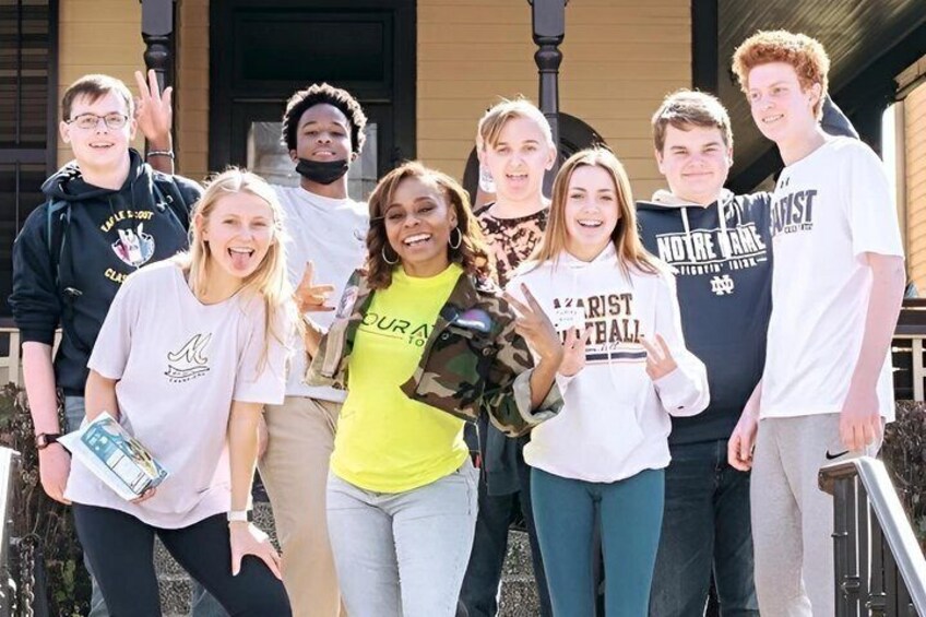 A group of people standing in front of a building with a porch. 1