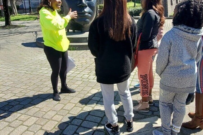 A group of people standing in a park with a large sculpture in the background. 2