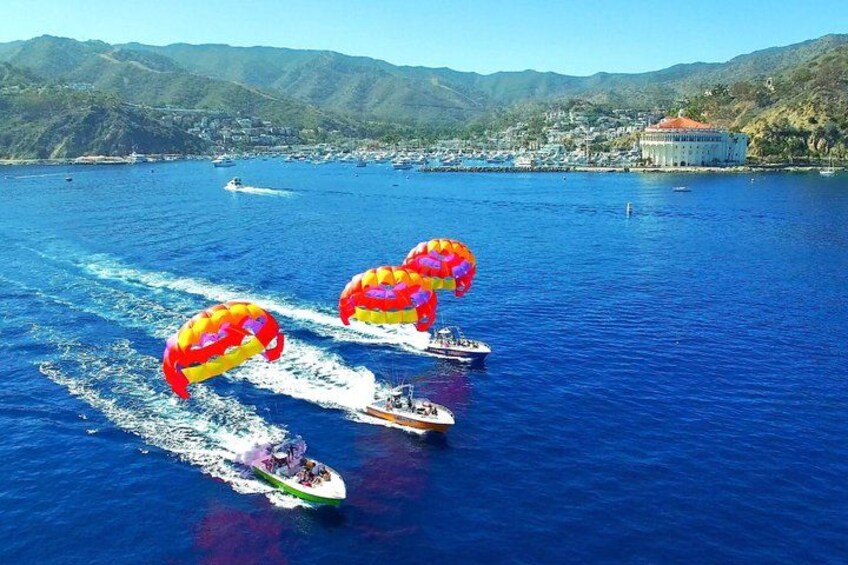 A parasailing activity with colorful parachutes over a body of water, a boat, and a mountainous landscape in the background. 2