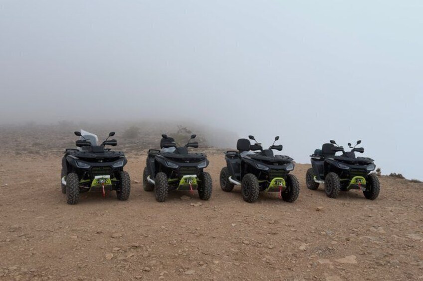 Four quad bikes parked on a dirt path in a foggy, mountainous area. 4