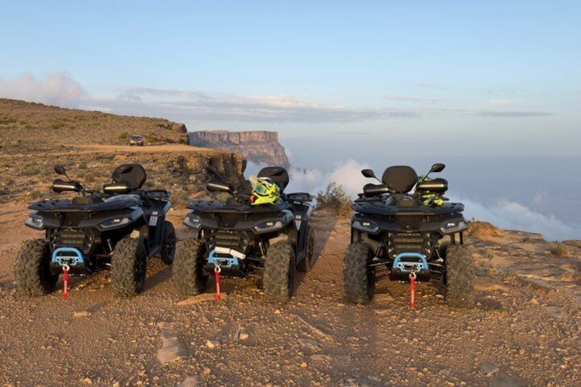 Three ATVs parked on a rocky terrain with a cliff in the background. 2
