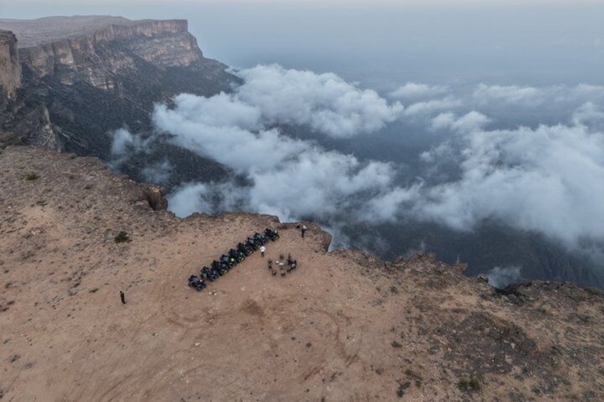 A group of motorcycles parked on a mountain ridge with clouds below. 3