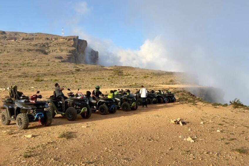 A group of ATVs parked on a dirt road with a rocky hill and a lighthouse in the background. 5