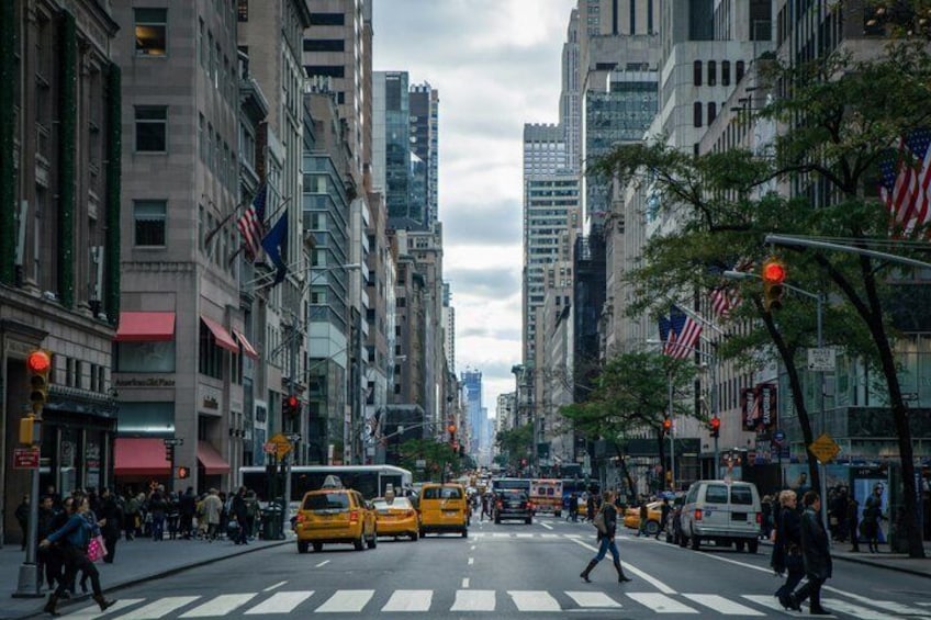 A busy urban street with tall buildings, yellow taxis, and pedestrians crossing at a crosswalk. 4