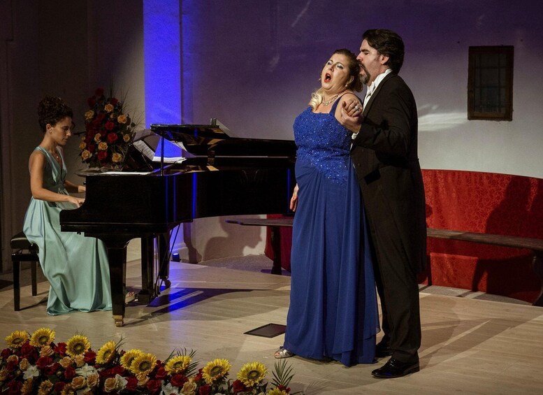 A stage with a piano, a woman in a blue dress, and a man in a suit. 5