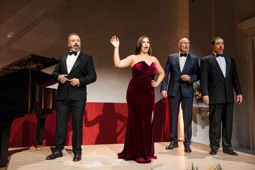 A formal event with four individuals on stage, one in a red dress, and a grand piano in the background. 2
