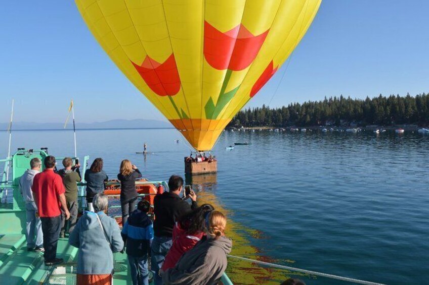 A hot air balloon with a colorful design, people on a boat, and a calm lake with trees in the background. 4