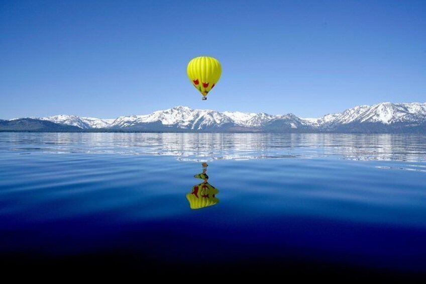 A yellow hot air balloon over a calm lake with snow-capped mountains in the background. 3