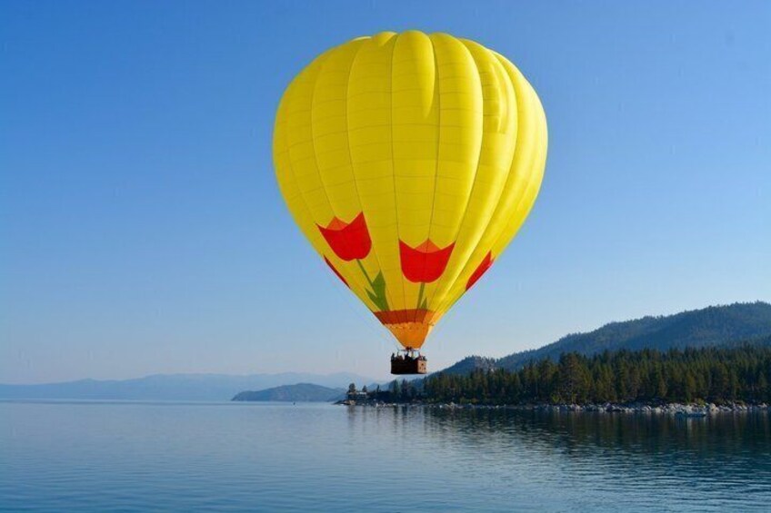 A yellow hot air balloon with red tulips over calm water with a forested island in the background. 2