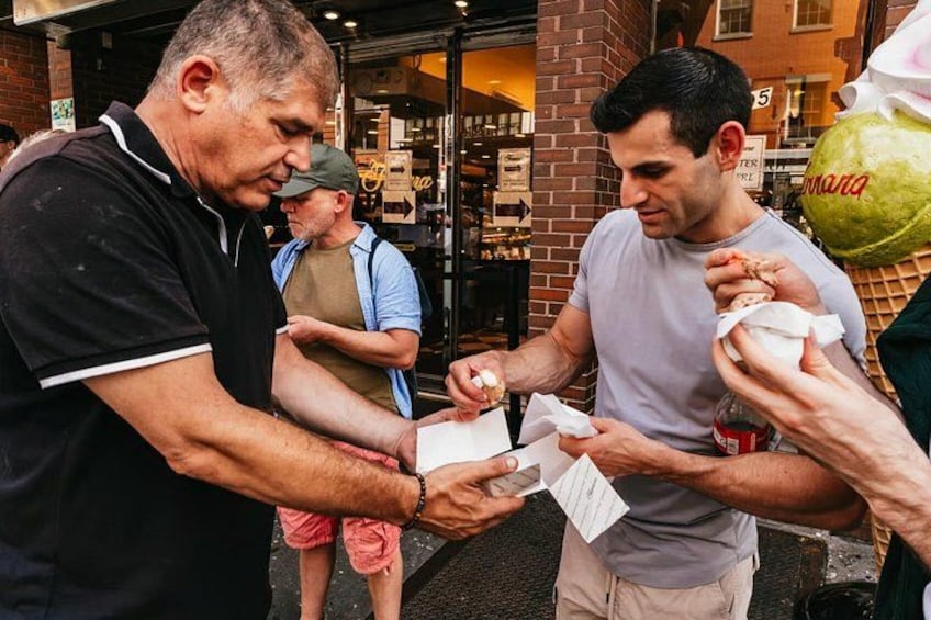 A street scene with people interacting, a brick building, and a green bag. 3