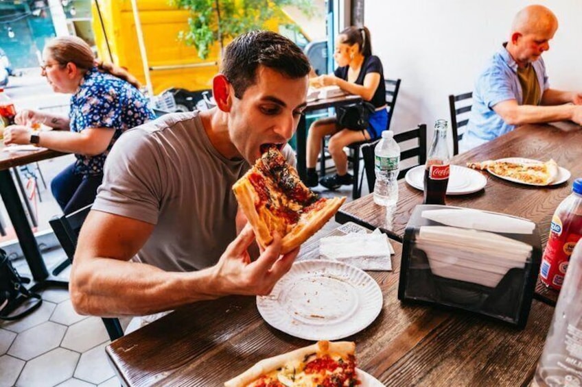 A person eating pizza at a restaurant table with other diners in the background. 1