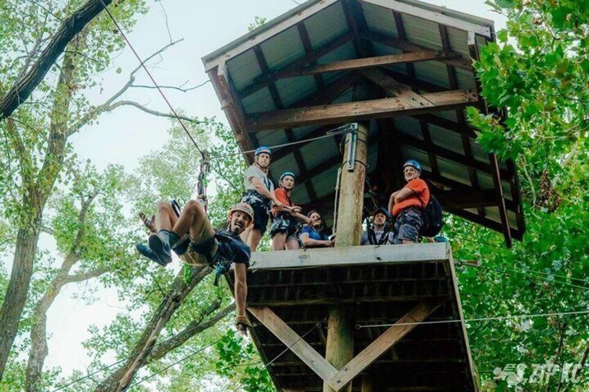 People on a zip line, trees, and a wooden platform. 2