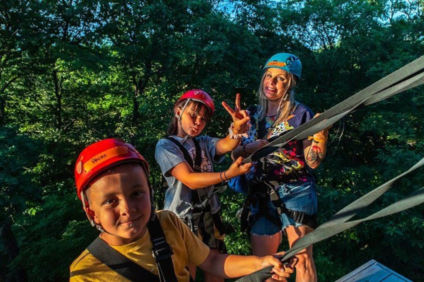 Three people wearing helmets and harnesses, engaged in a zip-lining activity in a forested area. 3