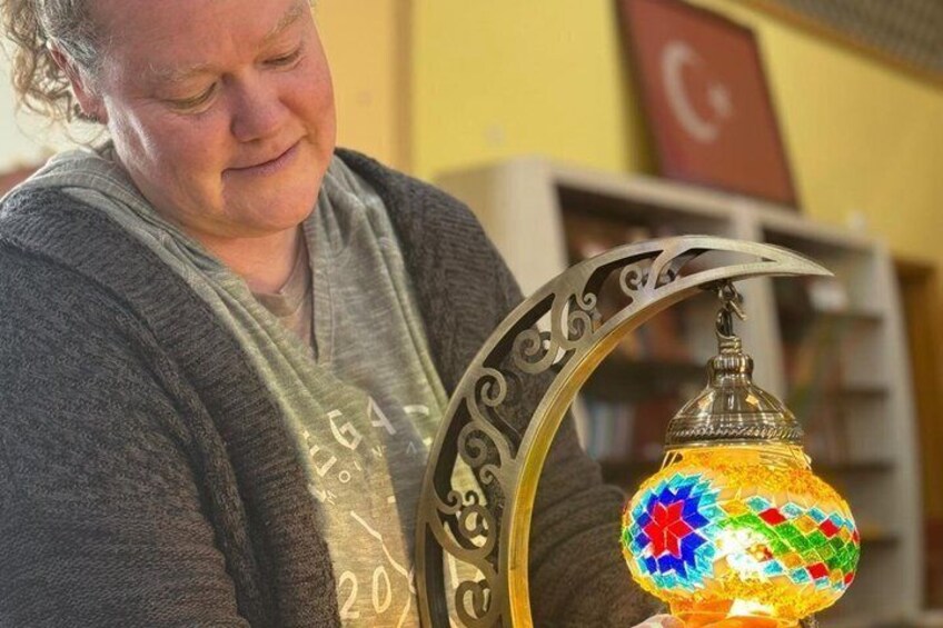 A person holding a decorative lamp with a metal frame and a colorful glass shade. 1