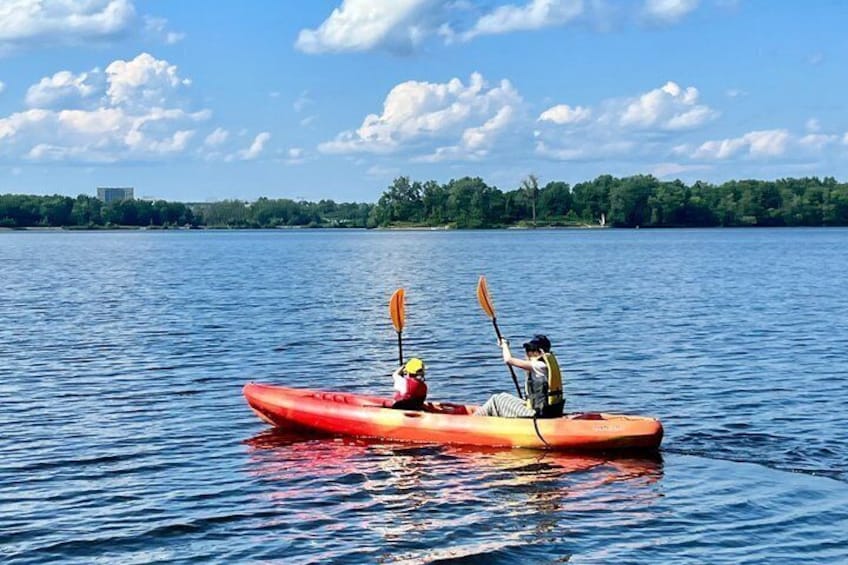 Two people kayaking on a calm lake with a clear sky and trees in the background. 5