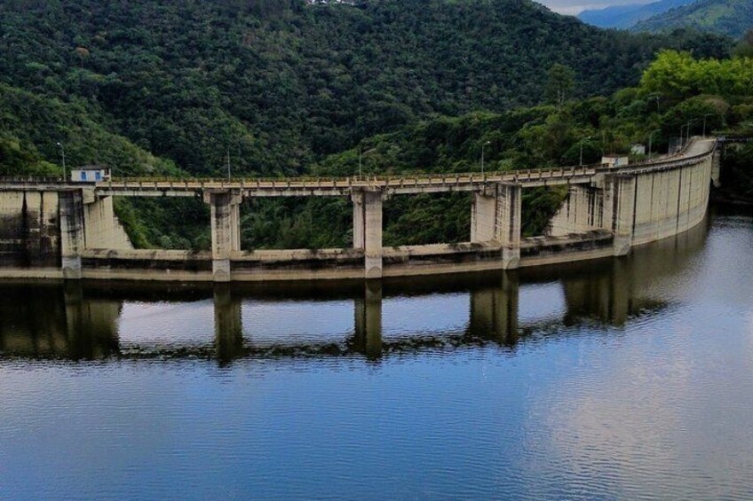 A dam with a bridge over a calm river, surrounded by lush green hills. 3