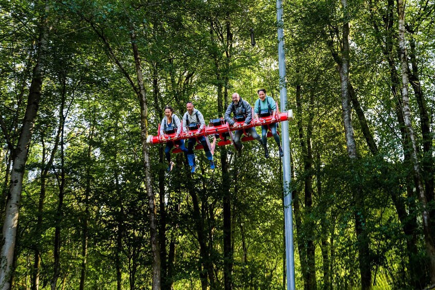 Four people on a red suspended bridge in a forest. 4