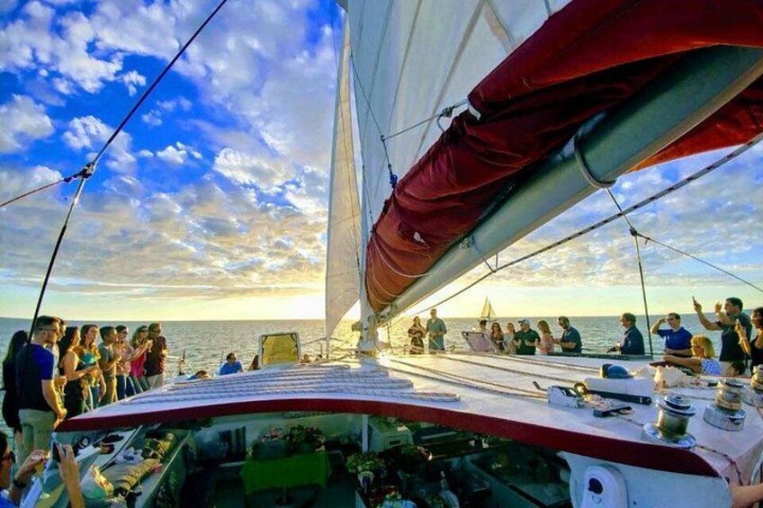A sailboat with people on deck, a clear sky, and the ocean in the background. 5