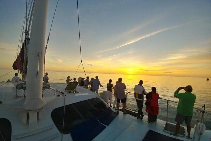 A sunset on a calm sea with a group of people on a sailboat. 4