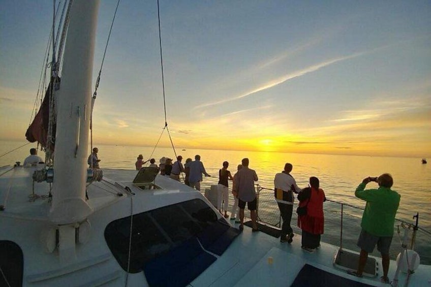 A sunset on a calm sea with a sailboat and people on the deck. 4