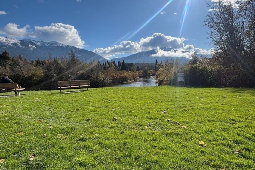 A grassy field with benches, a river, and mountains in the background. 4