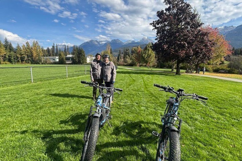 Two people standing next to bicycles in a grassy field with mountains in the background. 3