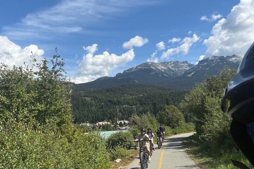 A mountain biking trail with riders, surrounded by forest and mountains. 2