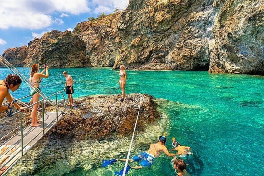 People swimming and standing on a rocky outcrop by clear turquoise water. 2