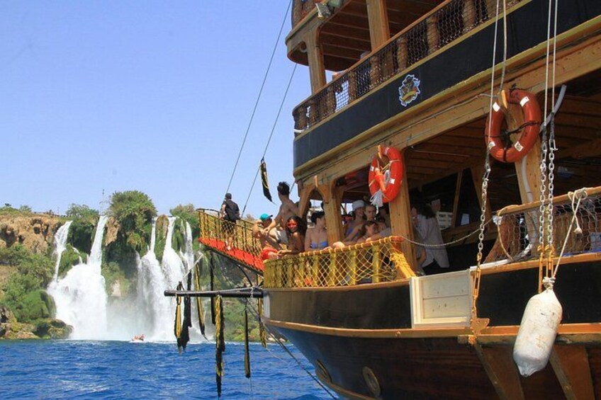 A boat with people on deck, a waterfall in the background, and a clear blue sky. 5