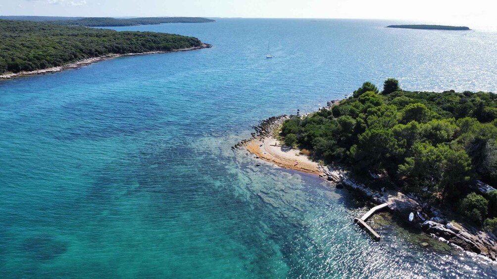 A coastal landscape with clear turquoise waters, a sandy beach, and dense green vegetation. 5