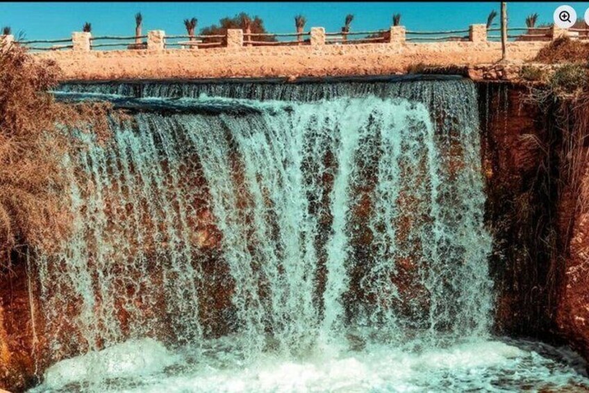 A waterfall cascading over a concrete barrier with a clear sky above. 1