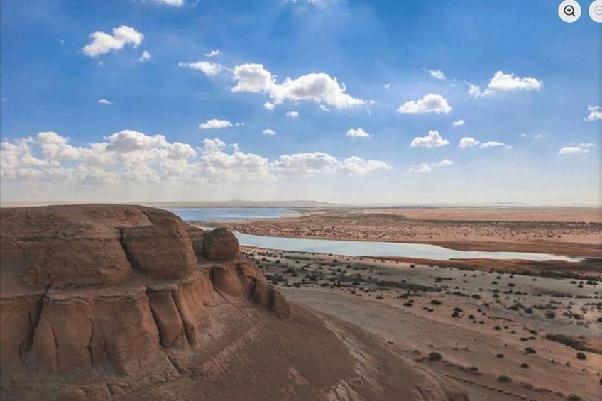 A desert landscape with a prominent rock formation and a distant body of water. 5