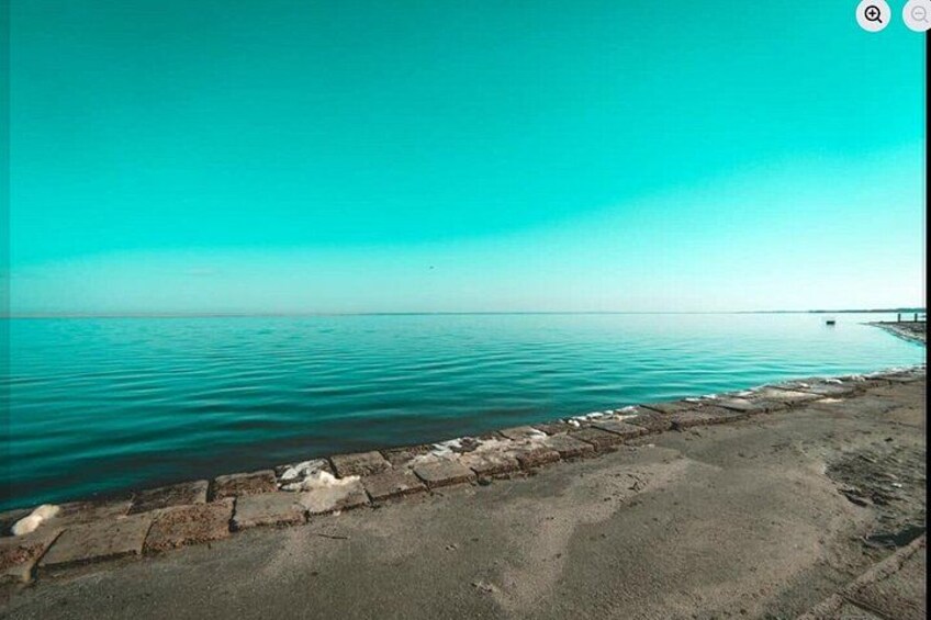 A calm sea with a clear sky, a concrete sea wall, and a distant pier. 4