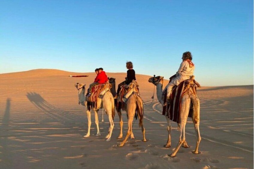 A group of people riding camels in a desert landscape. 2