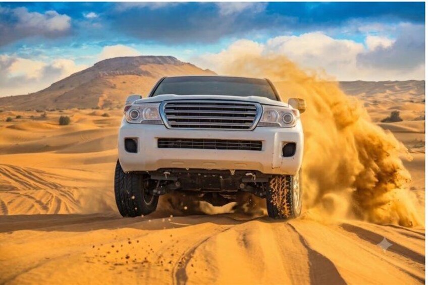 A white SUV driving through a desert with sand being kicked up by the tires. 1