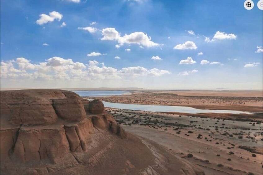A desert landscape with a prominent rock formation and a distant body of water. 3