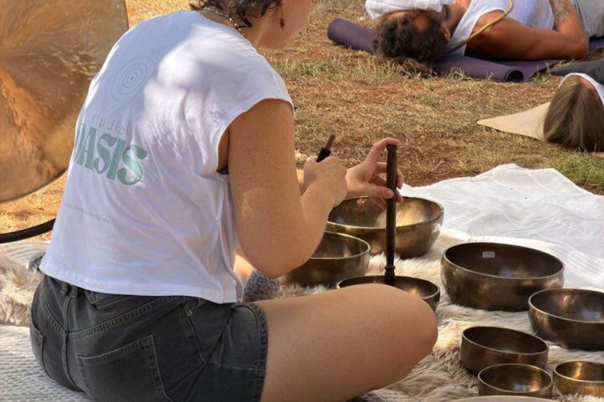 A person sitting on the ground with a meditation bowl, surrounded by other bowls and a mat. 2