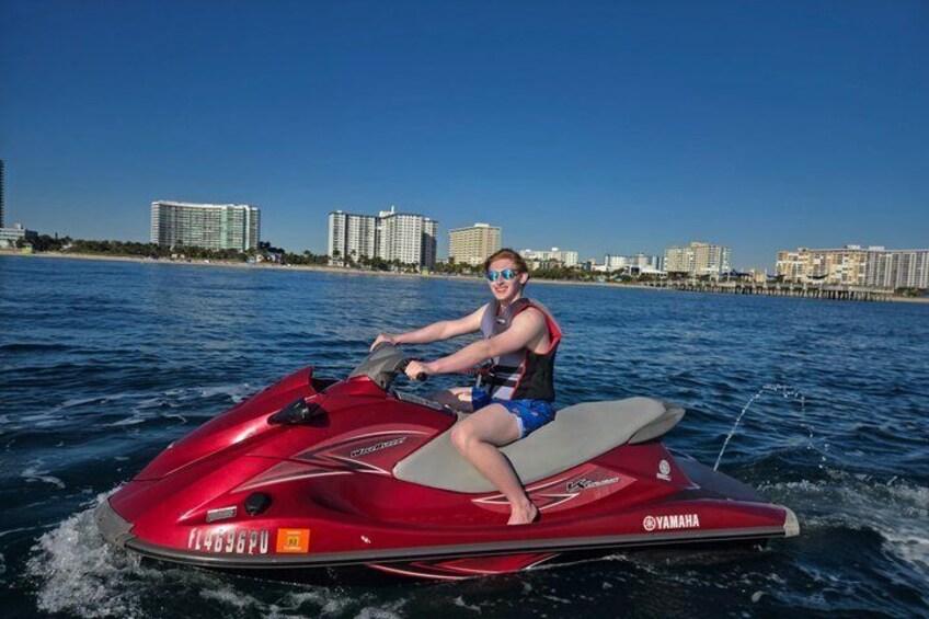 A person riding a red Yamaha jet ski on a body of water with a city skyline in the background. 4