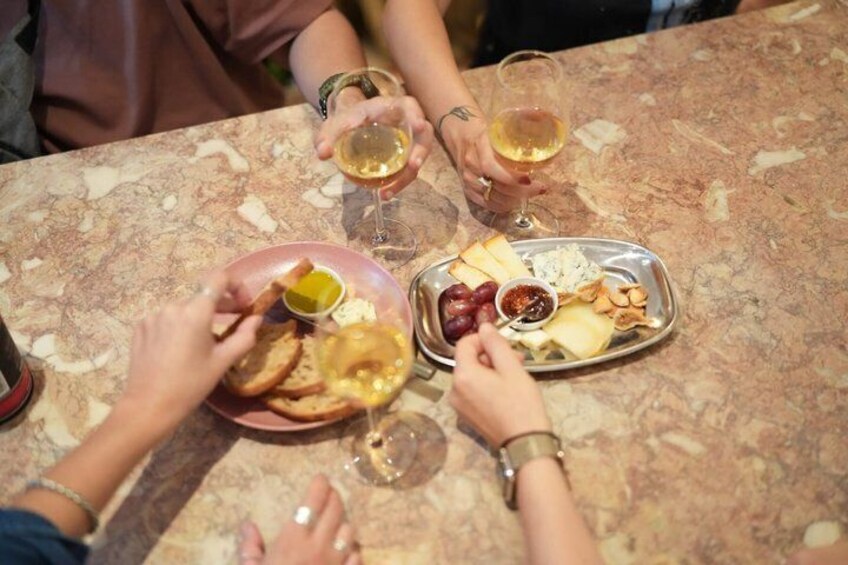 People toasting with wine glasses, sharing a meal with bread, cheese, and olives. 3