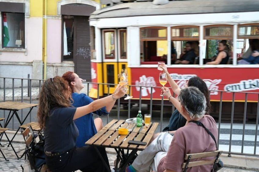 People toasting with drinks at a table with a tram in the background. 1