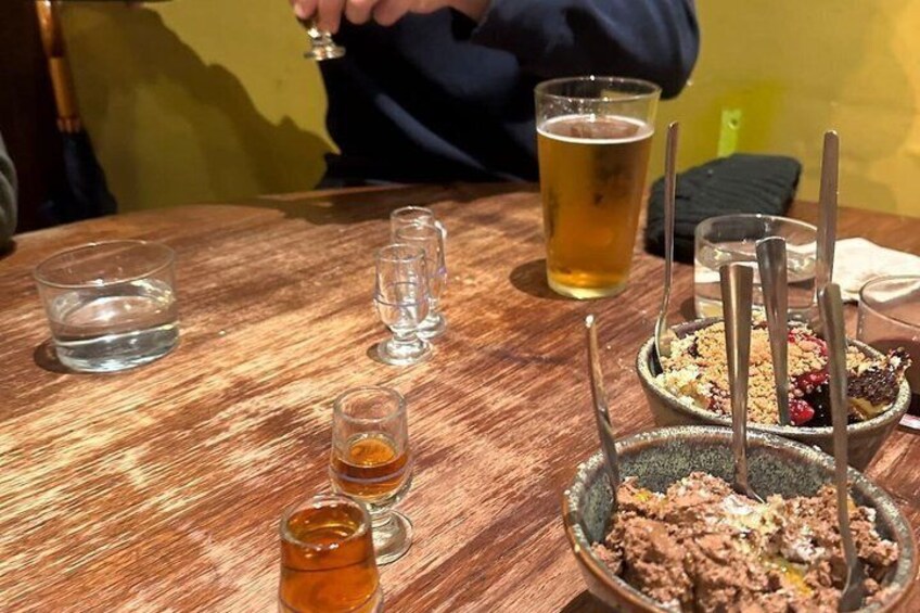 A wooden table with a glass of beer, shot glasses, and a bowl of food. 2